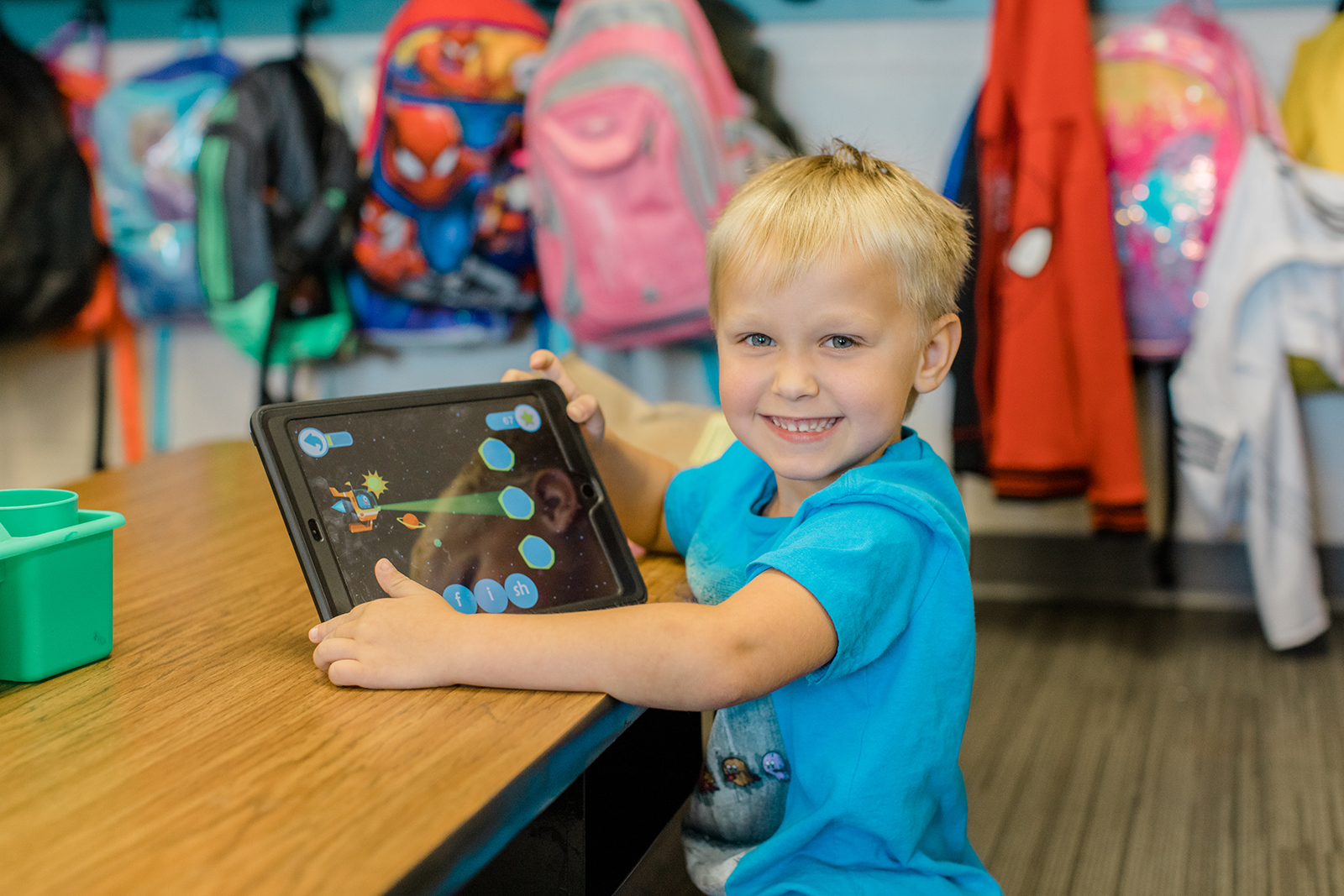 Preschool student smiles and holds up an ipad